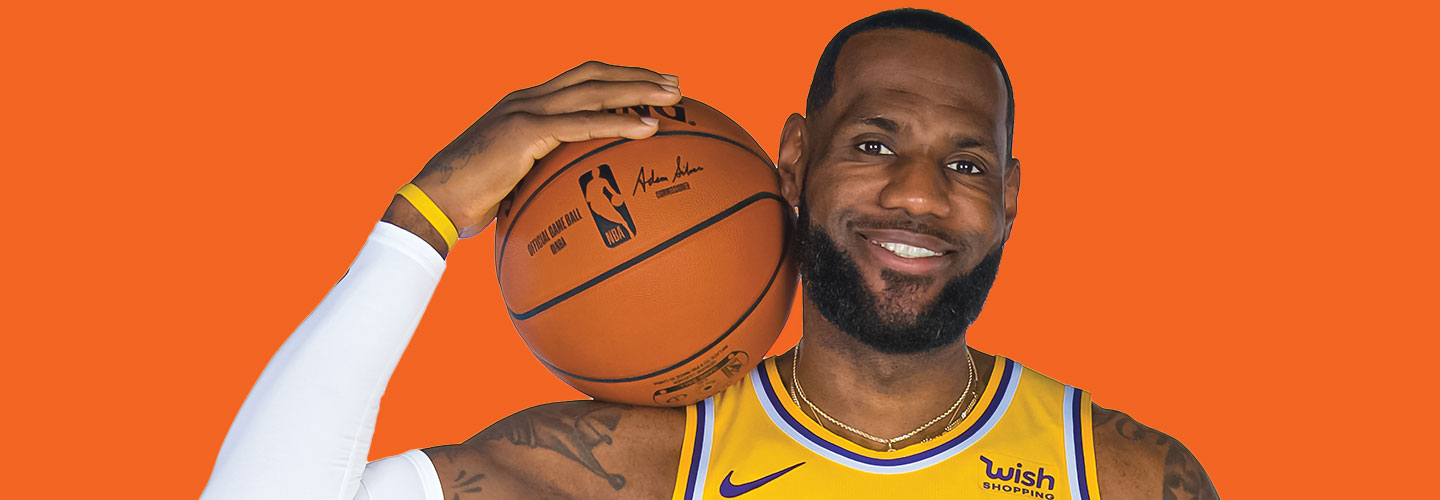 LeBron James smiling while holding a basketball in front of an orange background